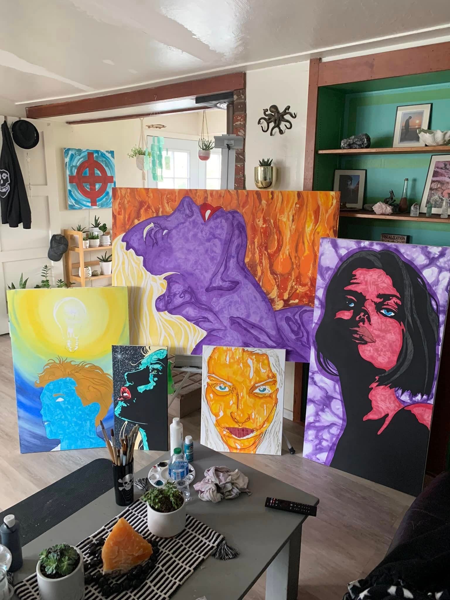 Six canvases propped together in the studio - portraits in purple, orange, yellow and pink.