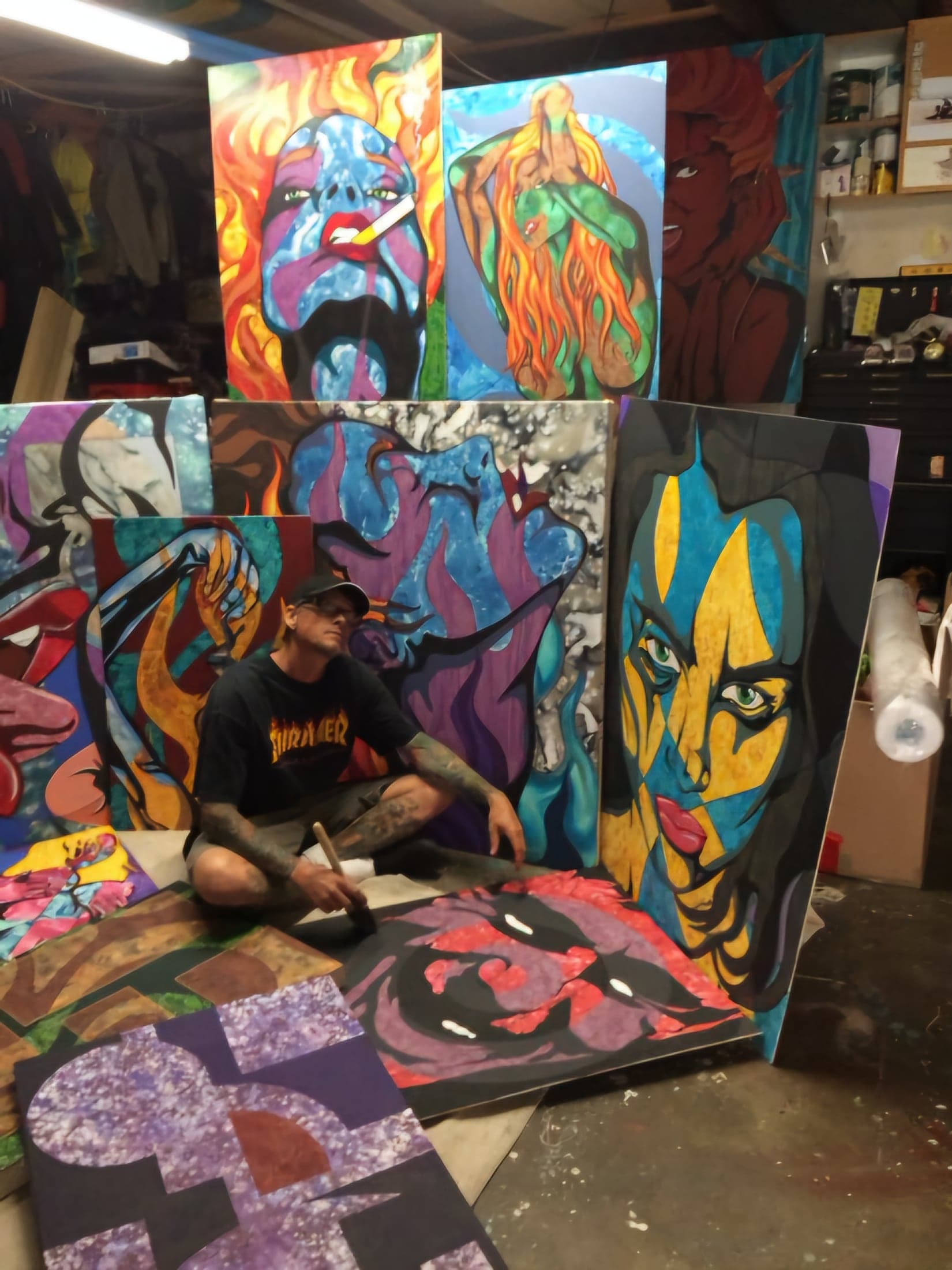 Sean sitting on the studio floor surrounded by a dozen finished canvases.