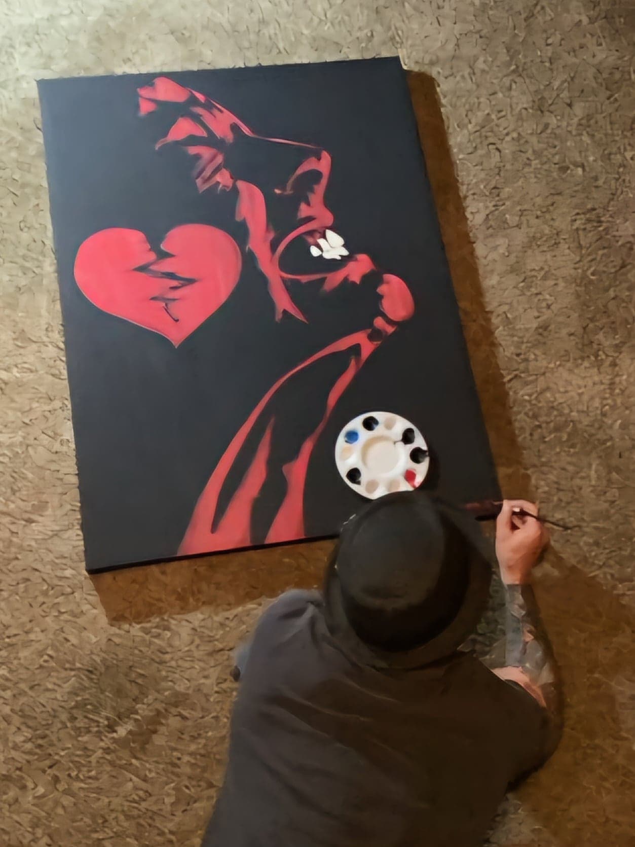 Sean painting the cracked-heart canvas flat on the floor, seen from above.