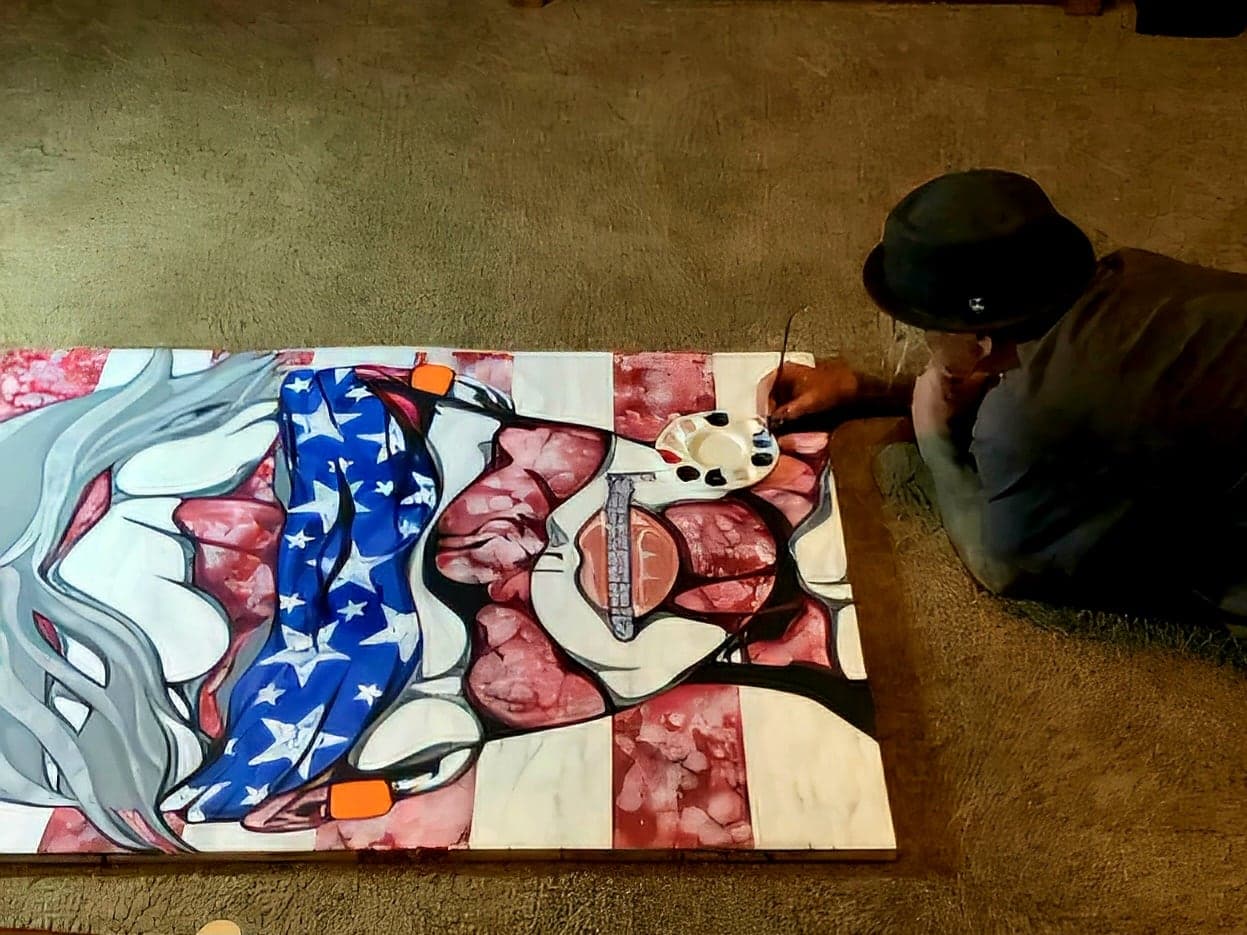 Sean painting the stars-and-stripes face canvas flat on the floor, seen from above.